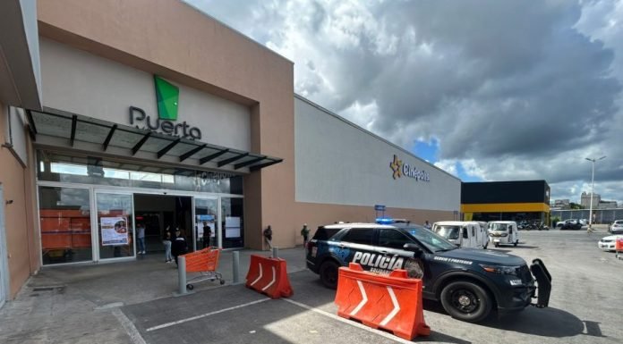 Exterior view of a shopping center named "P. Puerto" with a police vehicle parked outside and people entering the building.$# CAPTION