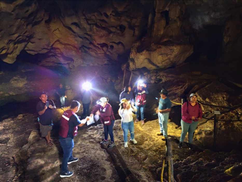 A group of people exploring a cave with flashlights in a dimly lit environment. Some individuals are interacting while others are capturing photos.$# CAPTION