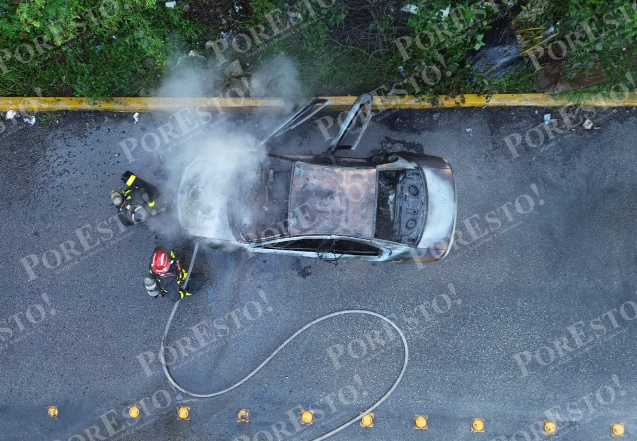 Firefighters extinguishing a car fire on a highway, with smoke rising from the vehicle and a fire hose in use.$# CAPTION