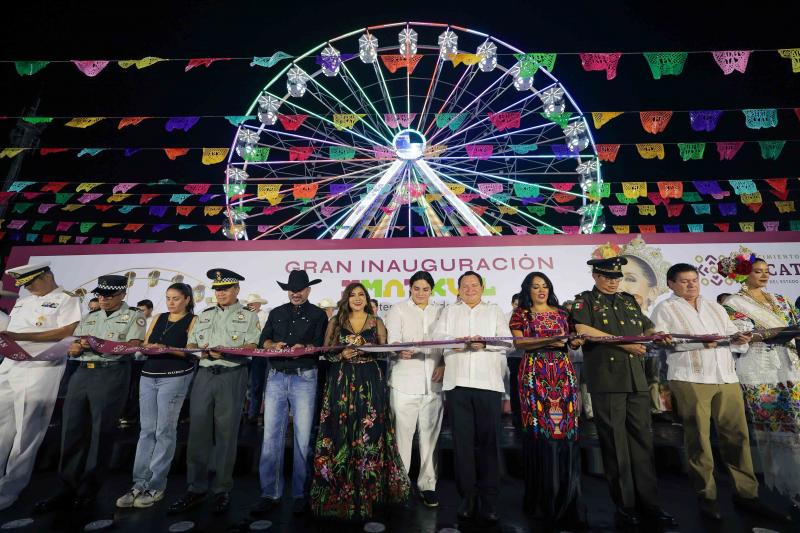 A ceremonial ribbon-cutting event featuring multiple individuals in traditional attire, with a ferris wheel illuminated in the background and colorful banners above.$#$ CAPTION