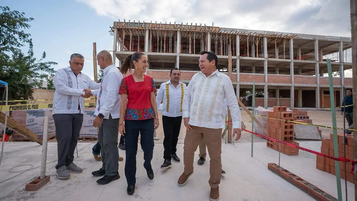 A group of officials engaged in discussions at a construction site, with a partially built structure in the background. They are wearing traditional and formal attire.
