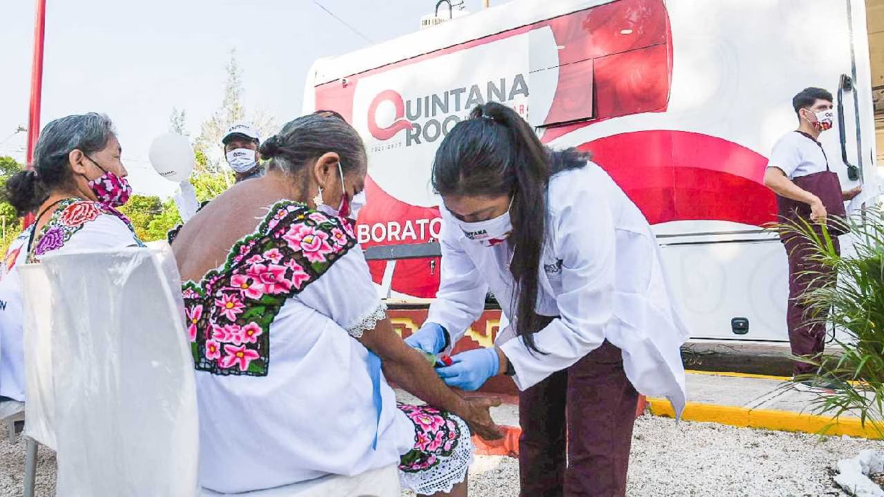 a healthcare worker gives a vaccination to an elderly woman in traditional attire in front of a mobile health unit