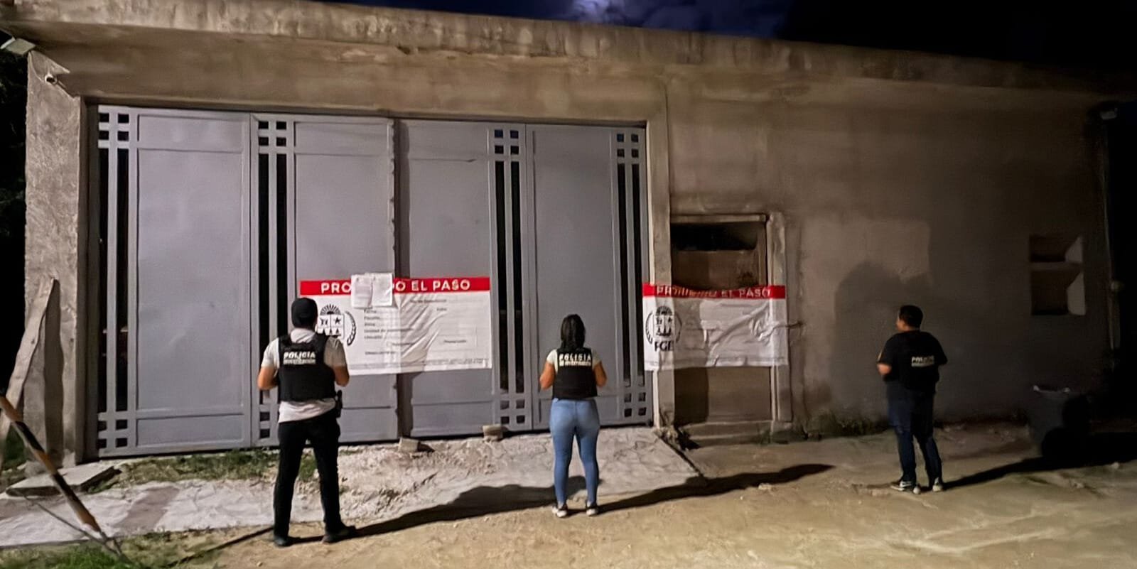 Three individuals facing a sealed entrance marked with official warning signs in low light conditions.$#$ CAPTION