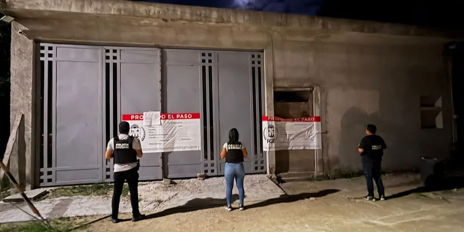 Three individuals facing a sealed entrance marked with official warning signs in low light conditions.$#$ CAPTION