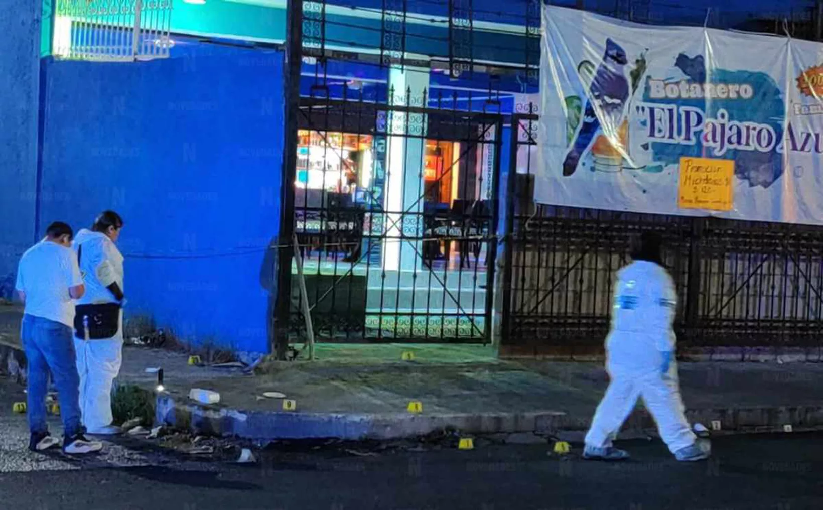 Crime scene investigation with forensic personnel examining evidence on the ground outside a business at night