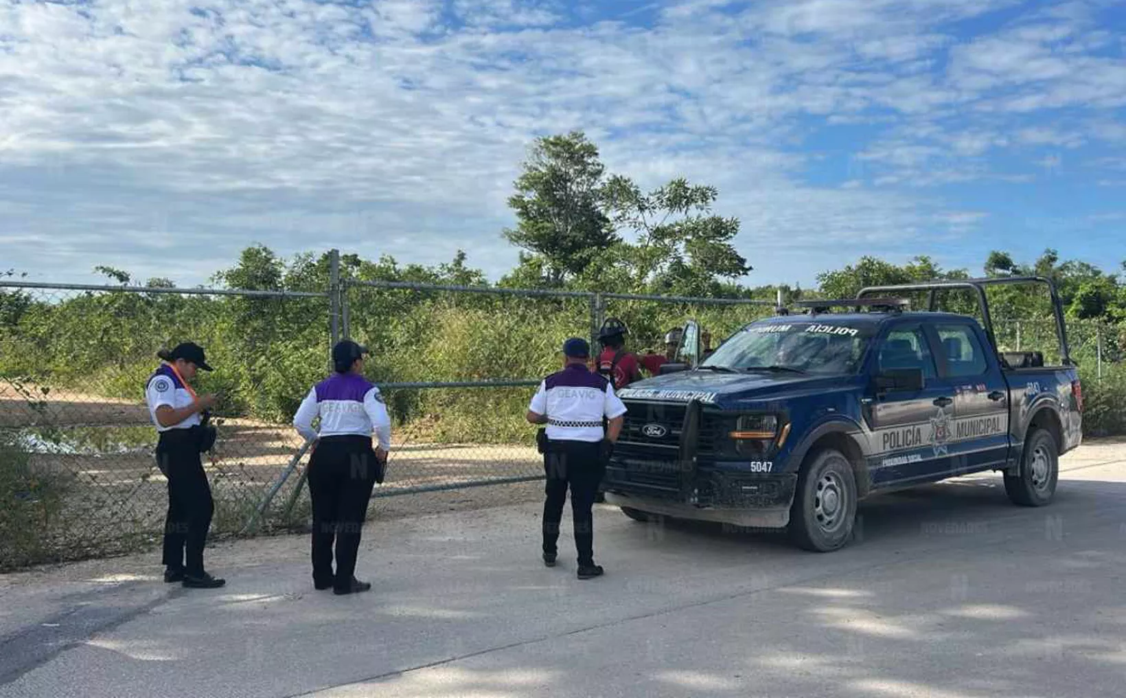 Local police officers inspecting a gate near a patrol vehicle in a rural area.$# CAPTION