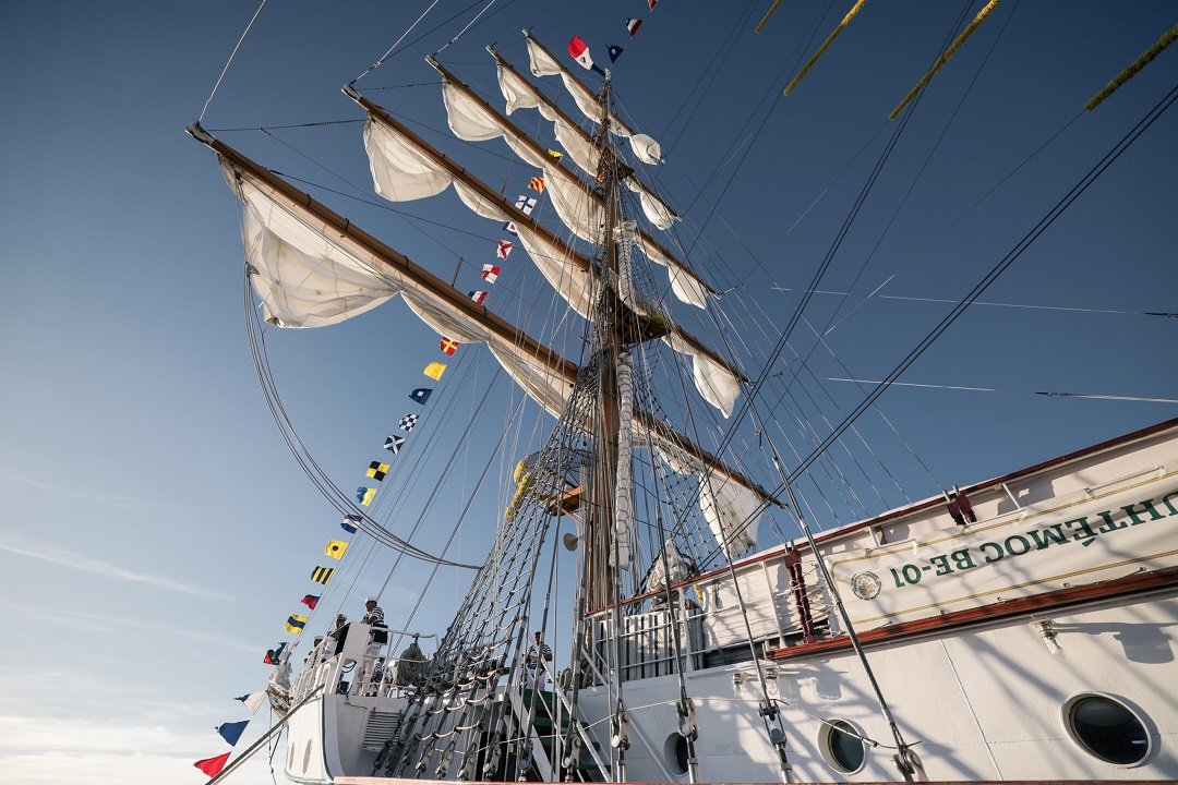 view of a tall sailing ship with sails and flags against a clear sky
