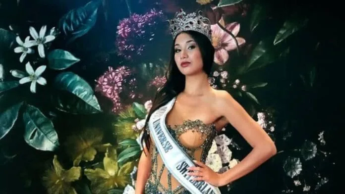 A beauty pageant contestant wearing a crown and sash, posing elegantly against a floral backdrop
