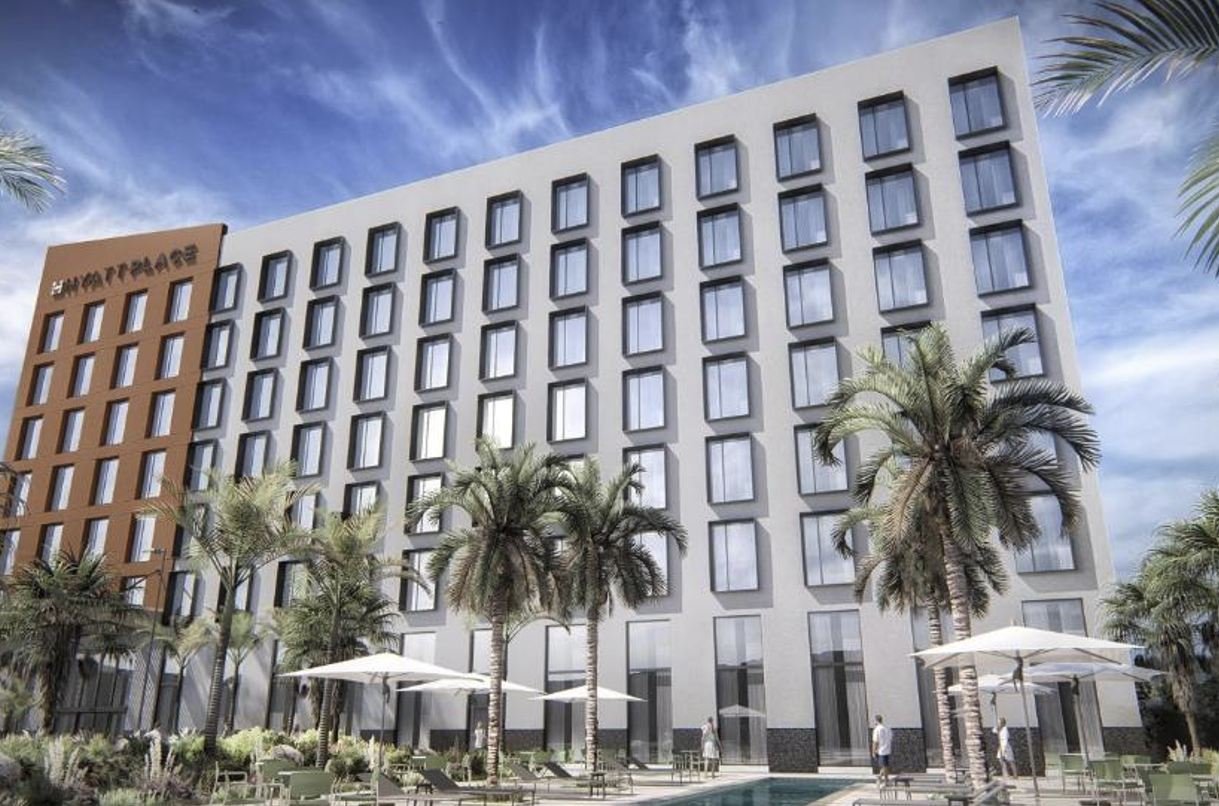 A modern hotel building with multiple windows and palm trees in the foreground, featuring outdoor seating and umbrellas by a pool area.$# CAPTION