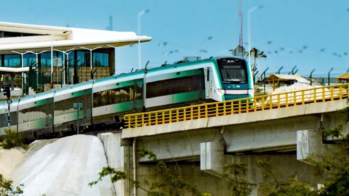 A modern train approaching a station on an elevated track with a bright blue sky in the background.$# CAPTION