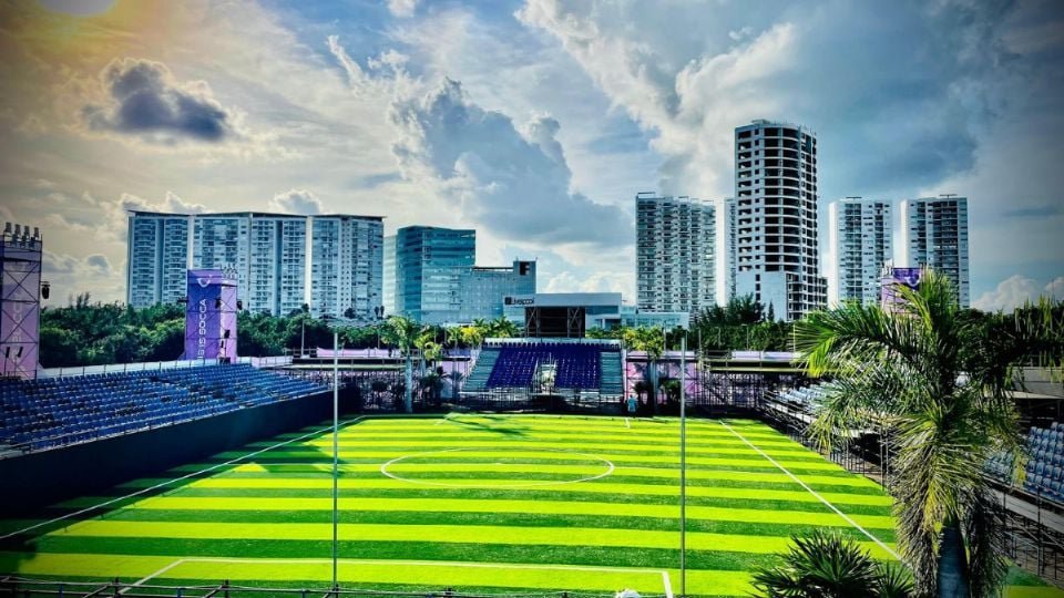 a vibrant soccer field with artificial turf surrounded by tall buildings and a clear sky