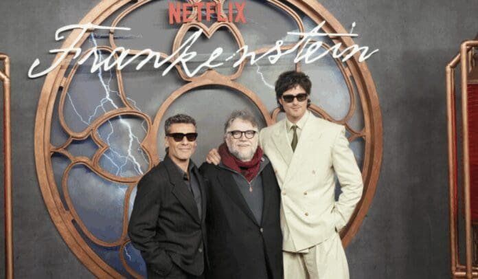 Three individuals posing together at the Netflix Frankenstein premiere event with a decorative backdrop
