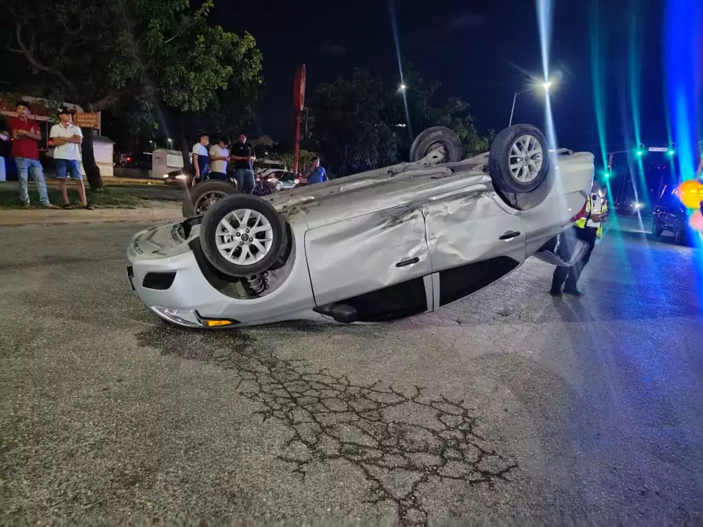 a silver car is overturned with its wheels in the air on a road while bystanders look on-$# CAPTION
