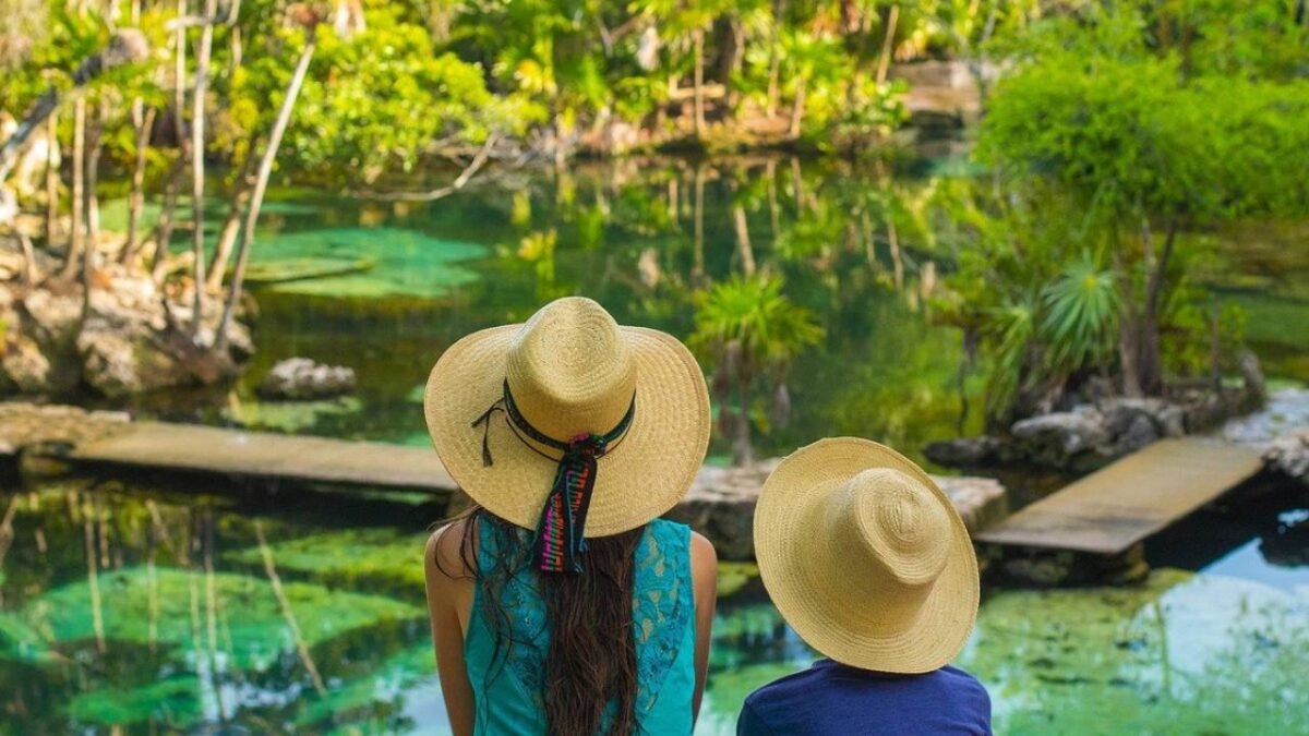 a woman and child wearing straw hats sitting by a serene water body surrounded by nature