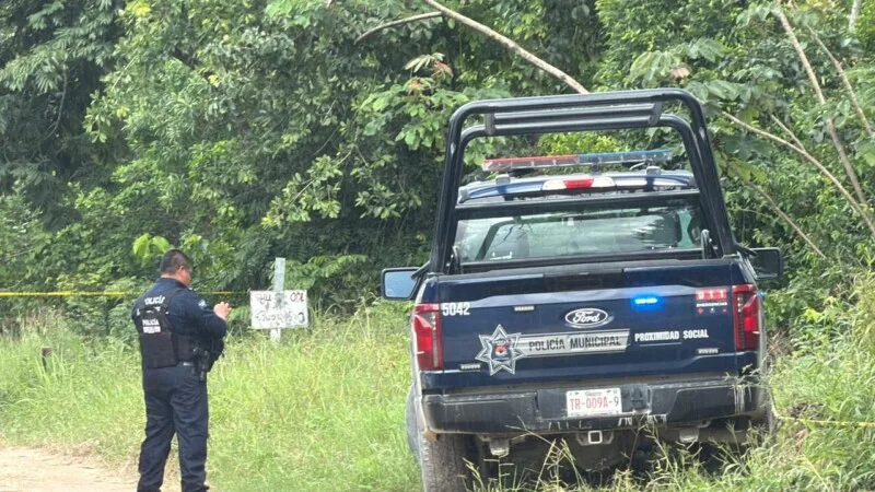 A police officer stands near a police truck in a green, rural setting with trees and grass surrounding the area.$# CAPTION