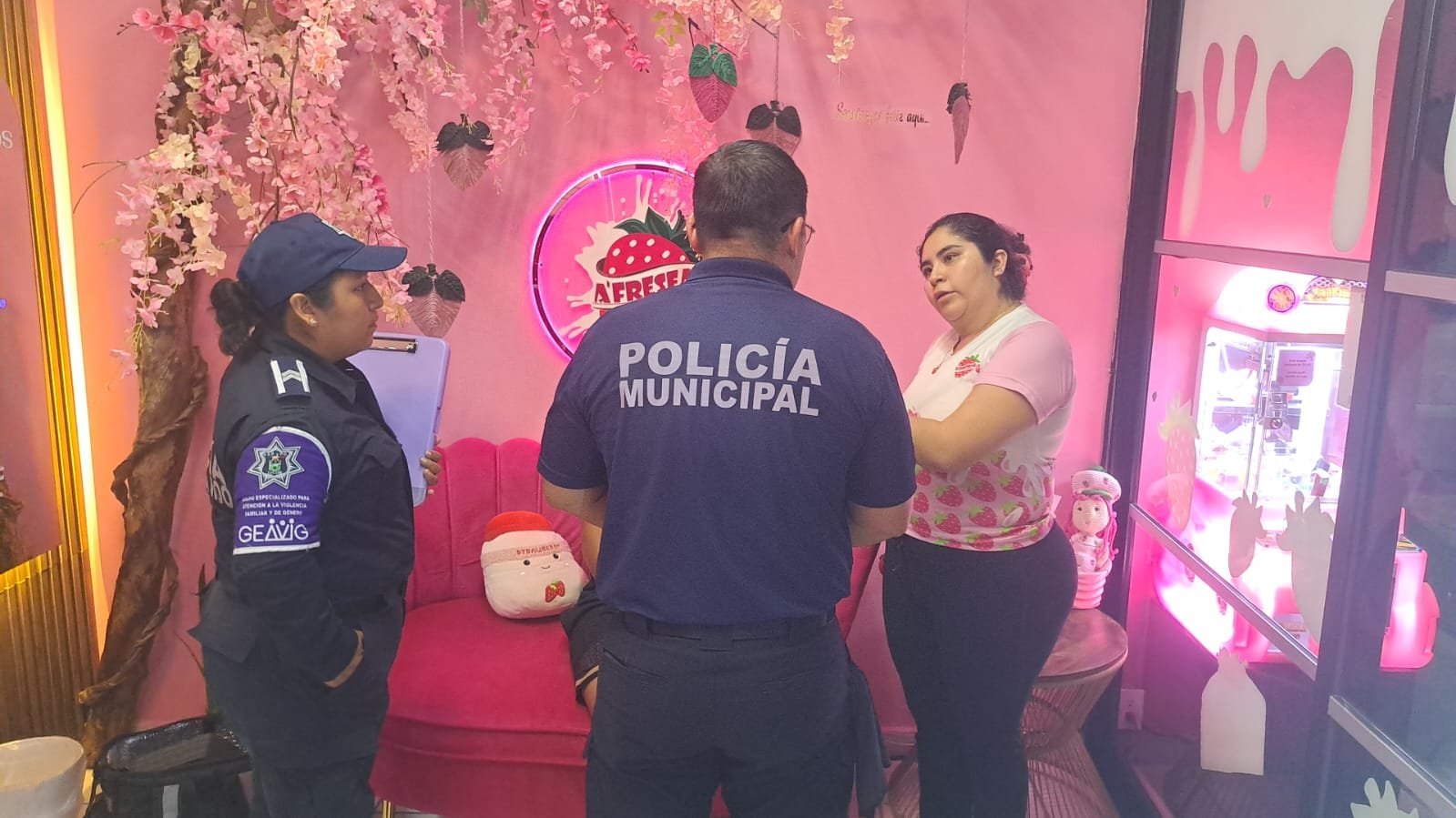 Municipal police officers discussing with a staff member inside a cafe decorated with bright colors and playful themes.$