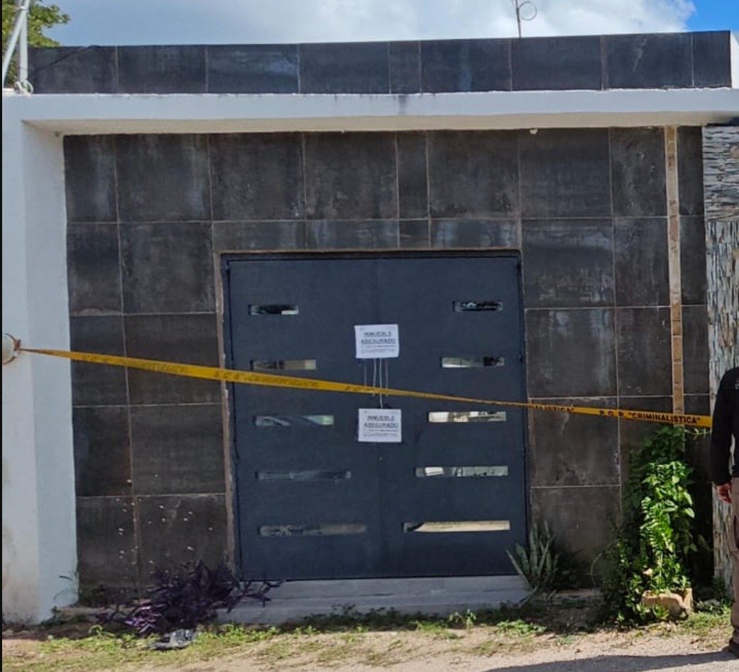 A closed gray door with warning tape and notices, indicating a secured property by authorities.$# CAPTION