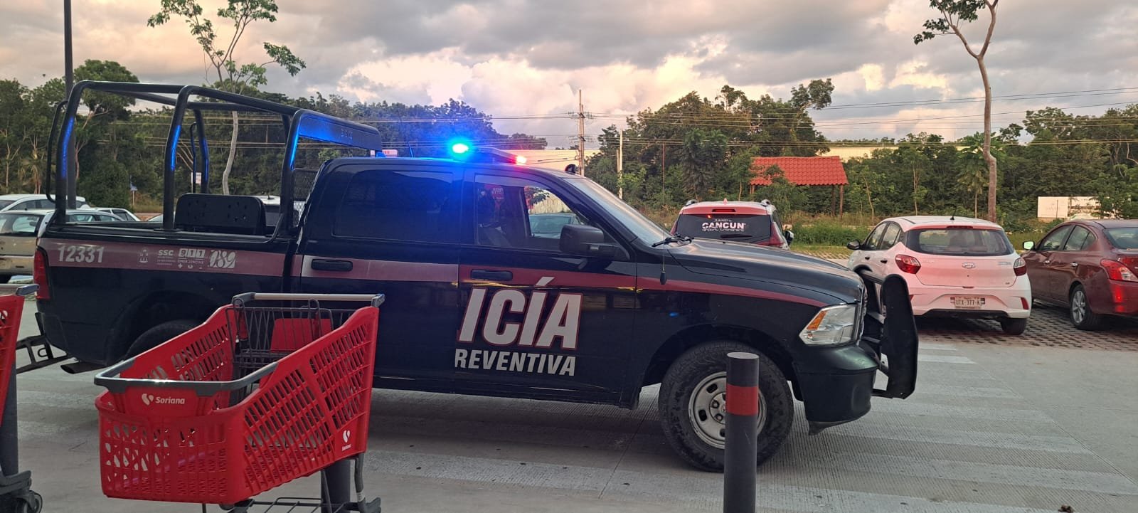 A police vehicle with blue and red lights parked in a shopping area, with shopping carts in the foreground and trees in the background.$# CAPTION