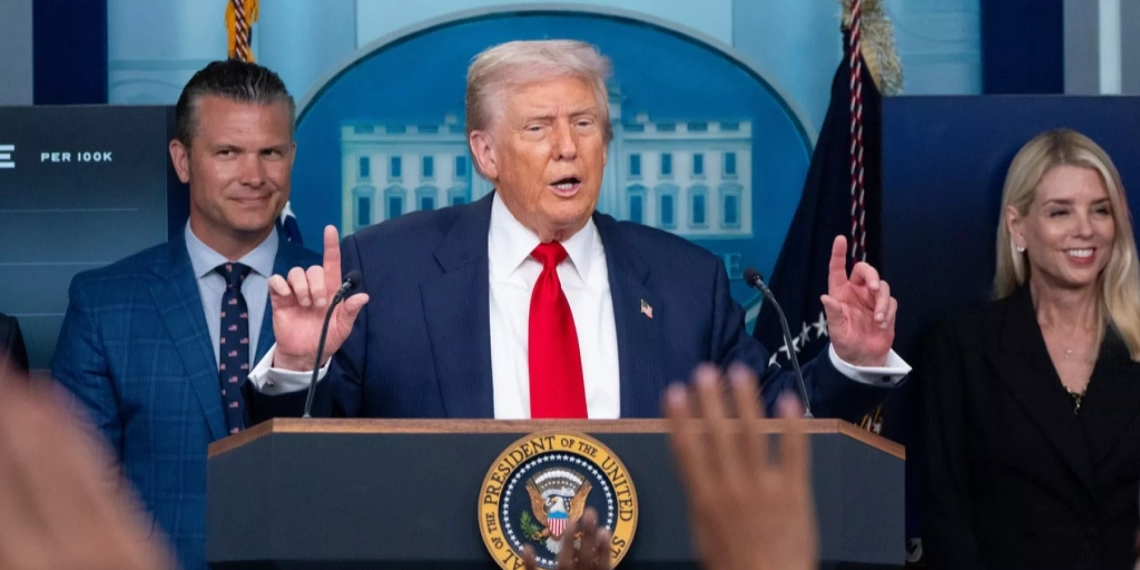 a man at a podium speaking during a press conference with two individuals standing beside him