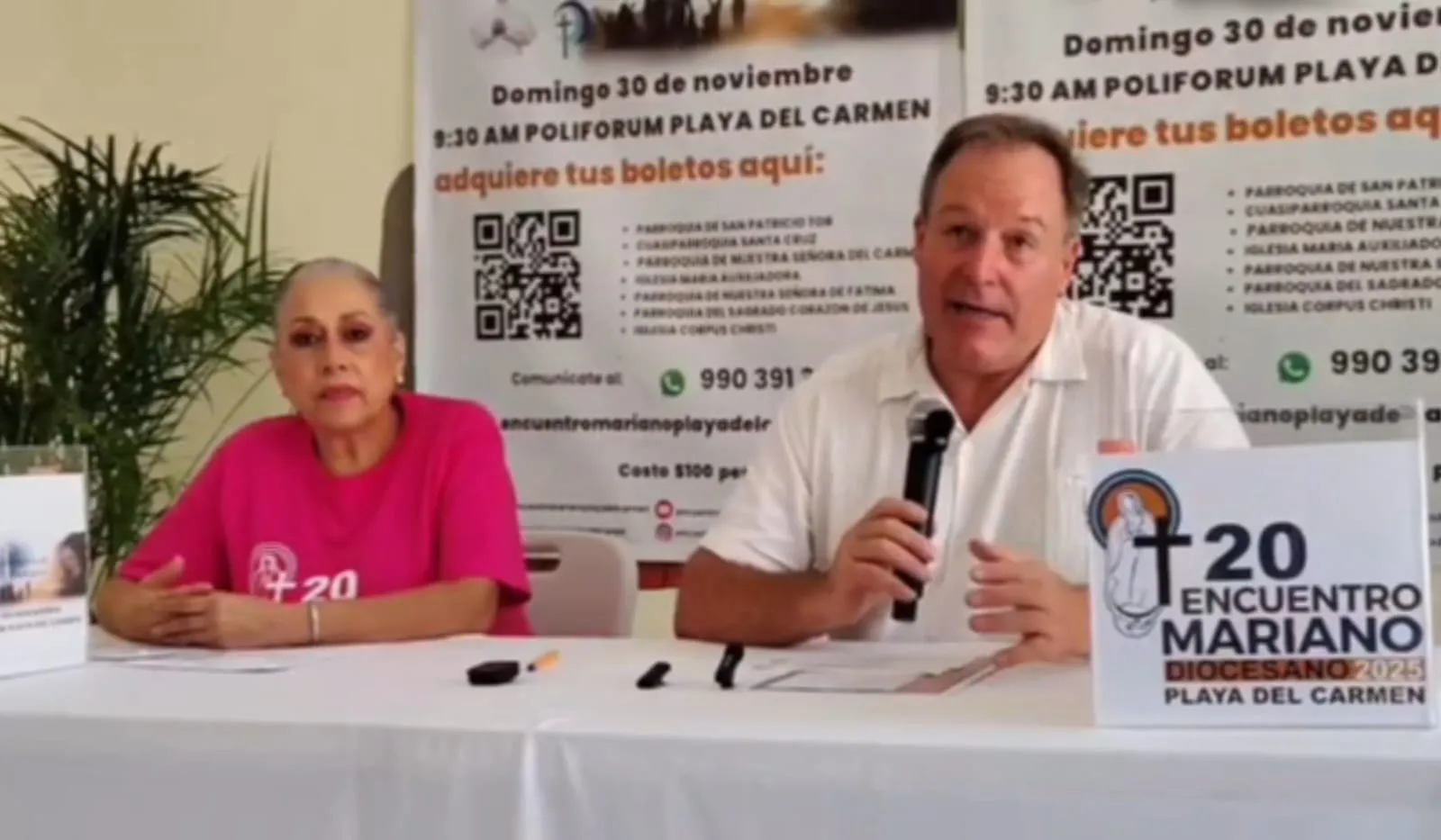 Two individuals speaking at a press conference with promotional materials for the 20th Diocesan Meeting in Playa del Carmen in the background.$# CAPTION