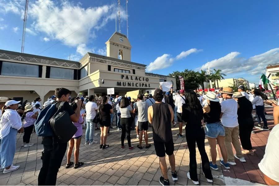 A crowd gathers outside the Municipal Palace for a demonstration under a bright blue sky with a few clouds.$#$ CAPTION