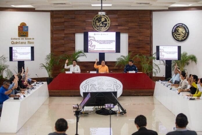 A government meeting in Quintana Roo with officials and attendees raising their hands for a vote or discussion.$#$ CAPTION