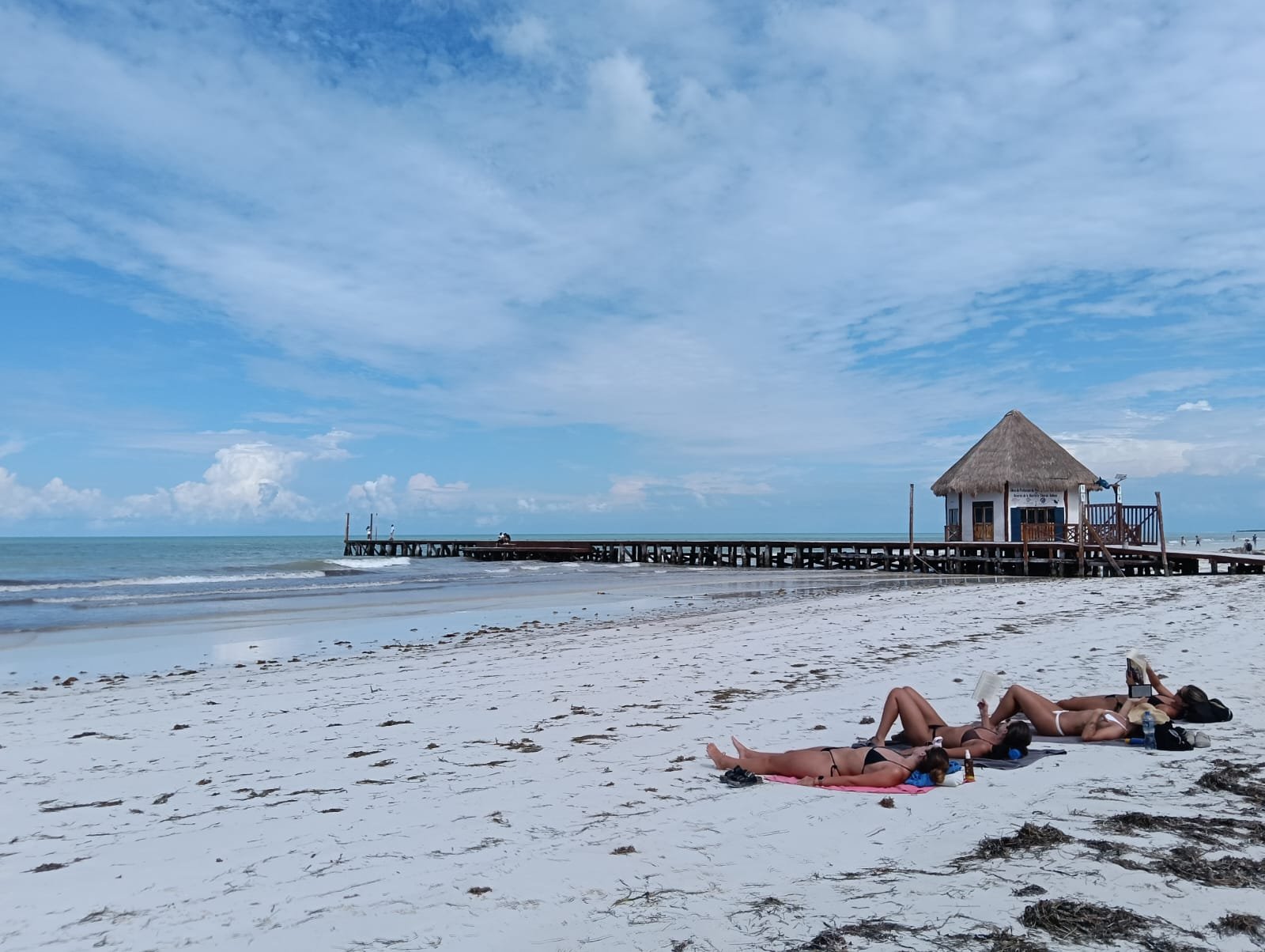 people sunbathing on the beach near a wooden pier under a blue sky