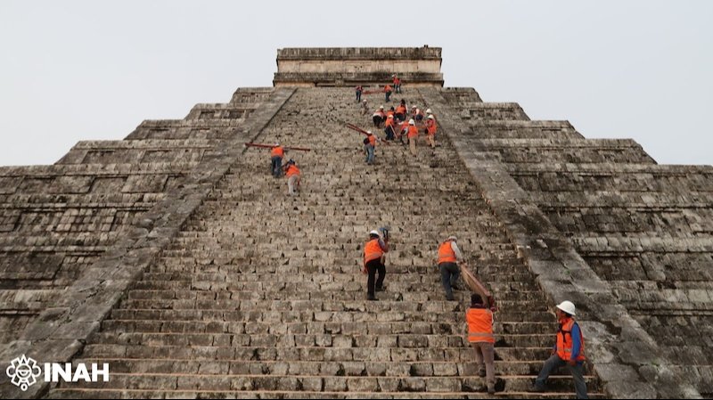 Workers climbing the steps of a Mayan pyramid during restoration efforts, wearing safety gear and orange vests