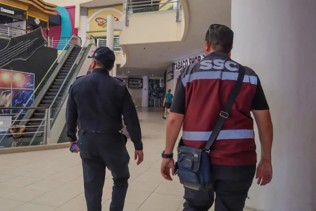 Two security personnel walking through a shopping mall, with a staircase and colorful decor in the background.$# CAPTION