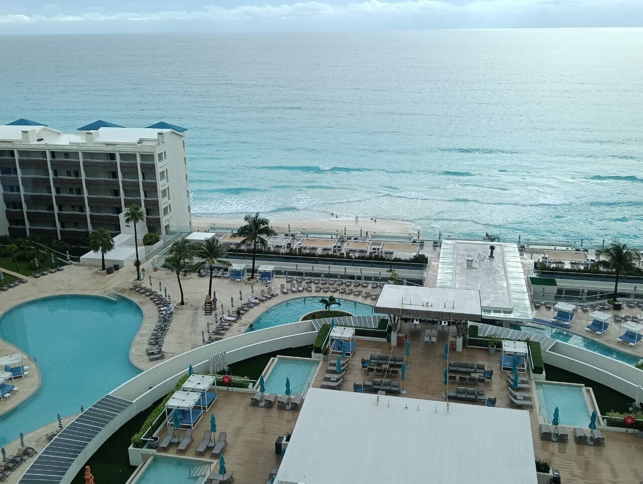a panoramic view of a beachfront resort featuring pools and palm trees with the ocean in the background