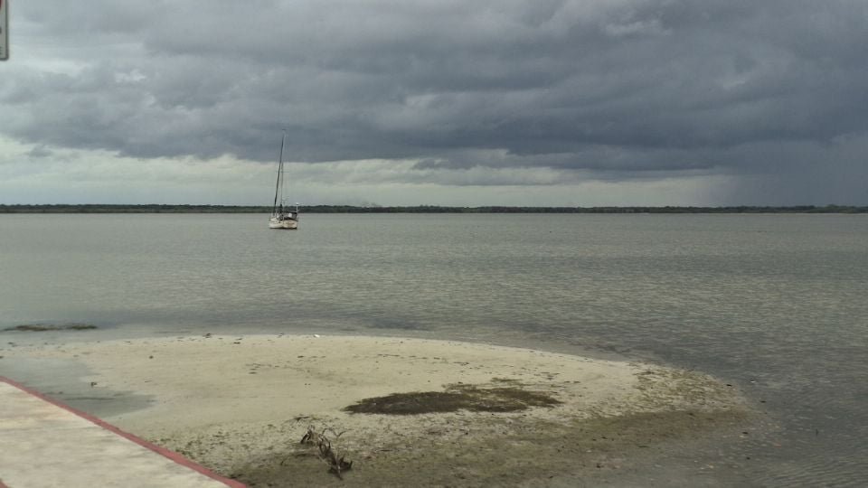a sailboat floating on calm waters near a sandy shore with dark clouds overhead