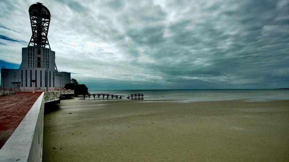 a coastal landscape featuring a unique building and a pier under a cloudy sky