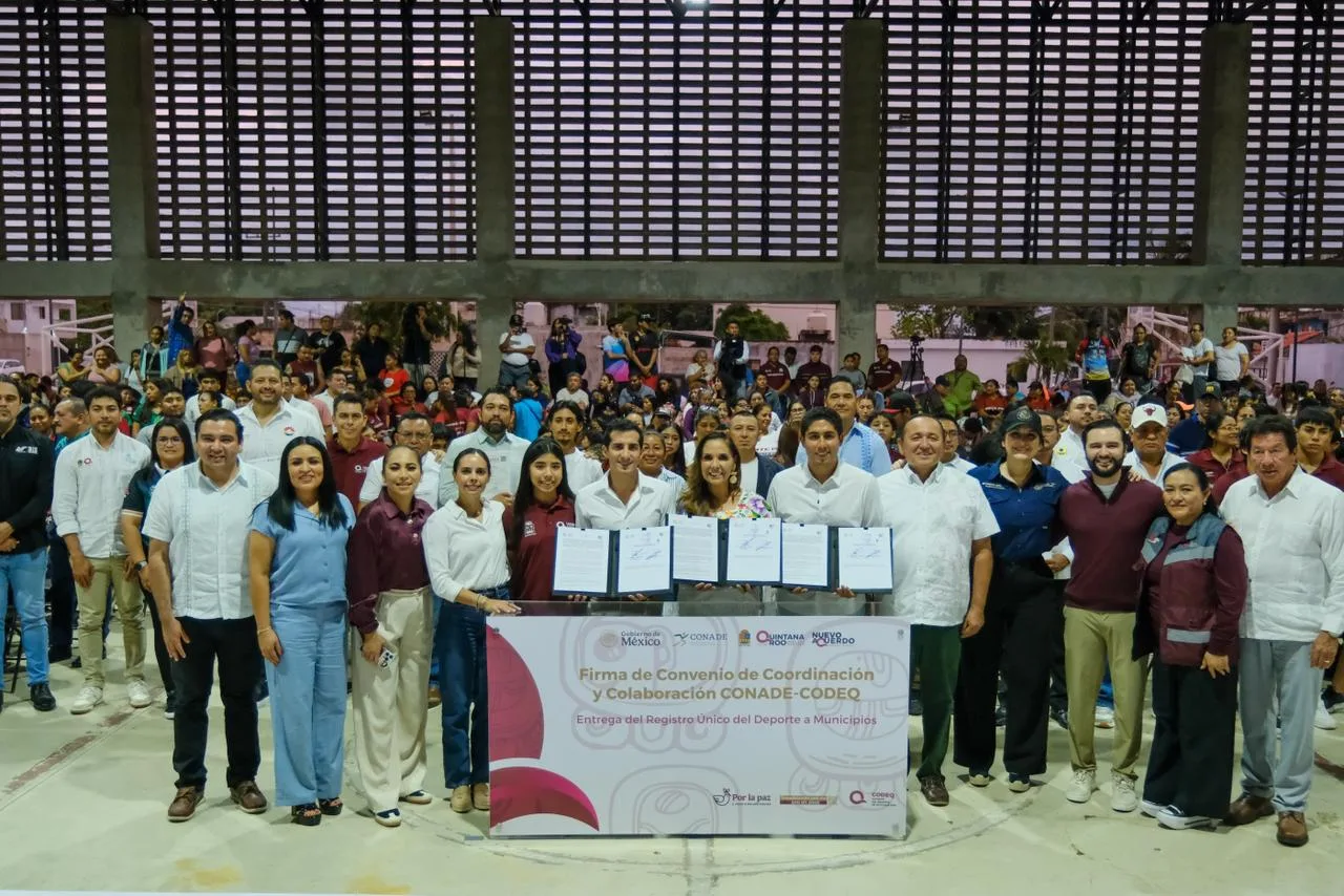 A group of officials and attendees at a signing event for a sports collaboration agreement, with a large audience in the background.$# CAPTION