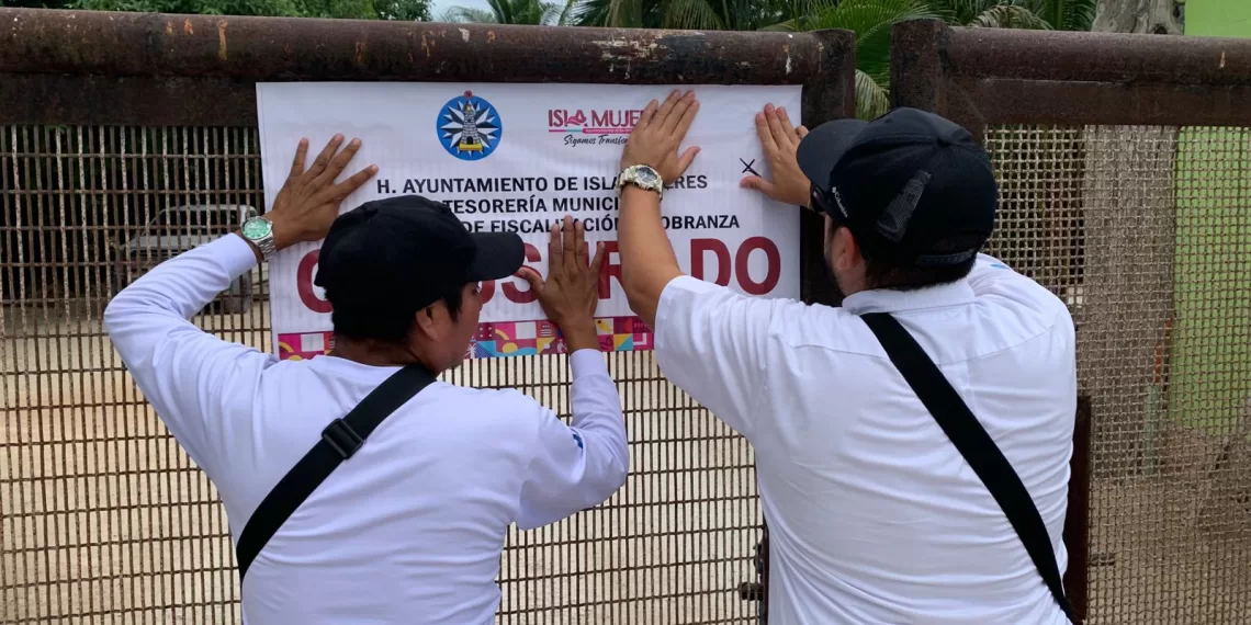 Two individuals attaching a sign to a fence at Isla Mujeres