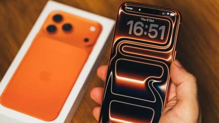 A person holding a smartphone displaying a digital clock and vibrant wallpaper, with an orange phone box in the background