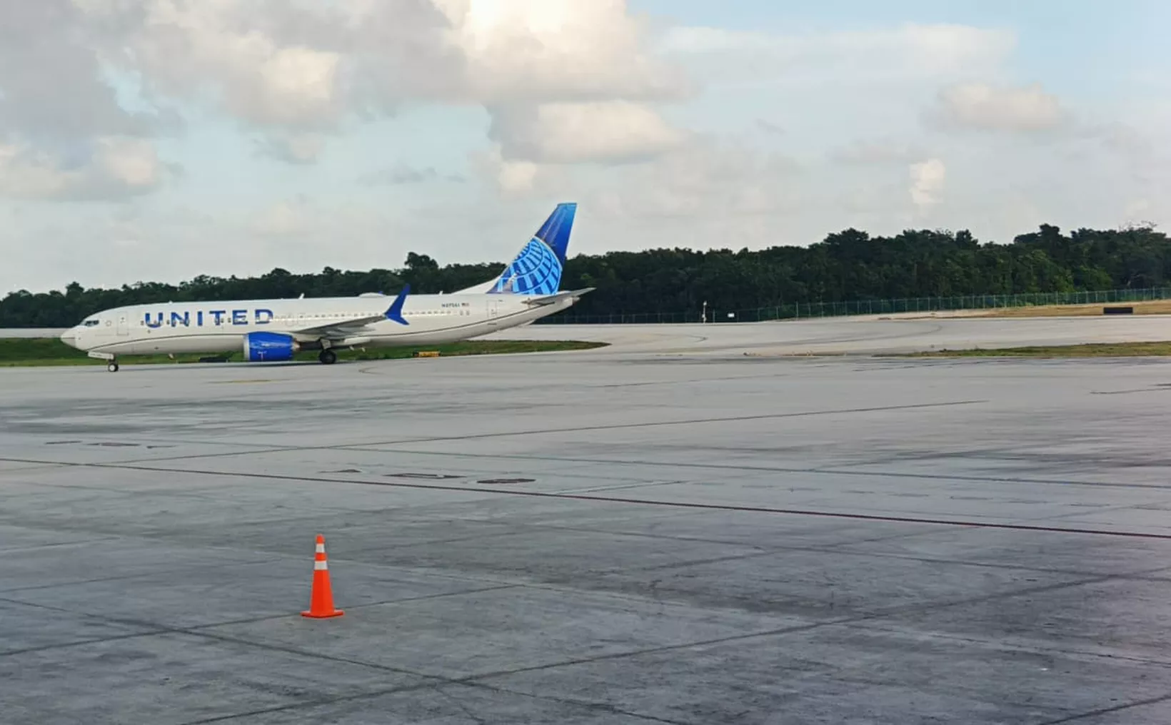 A United Airlines Boeing 737 aircraft taxiing on an airport runway with a clear sky and trees in the background.$# CAPTION