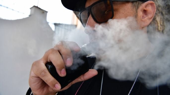 a man exhaling vapor from a vape device wearing sunglasses and a black outfit
