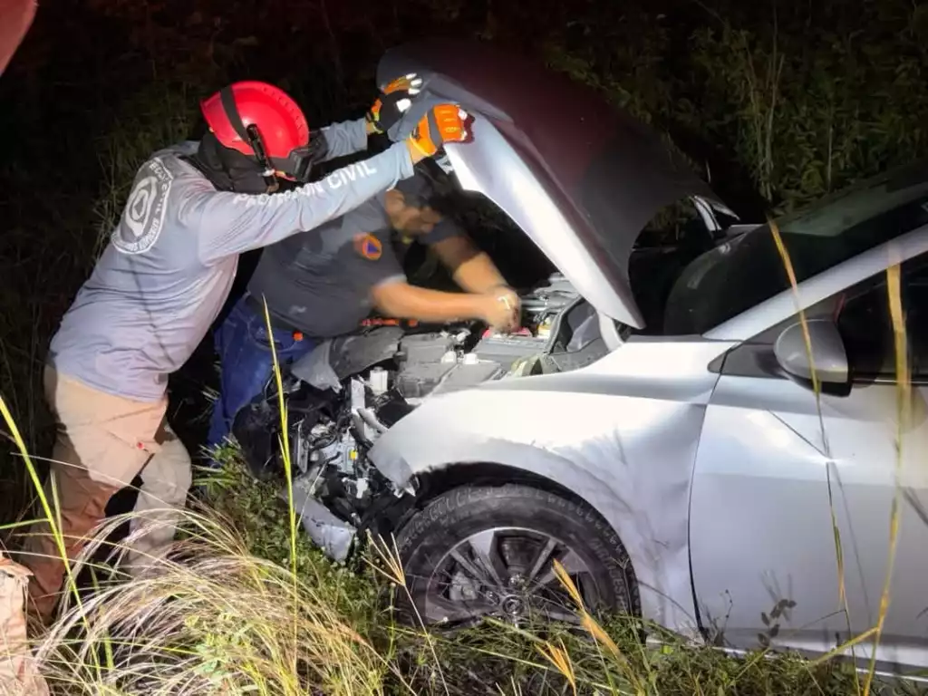 two individuals working on a car with its hood raised in a grassy area at night