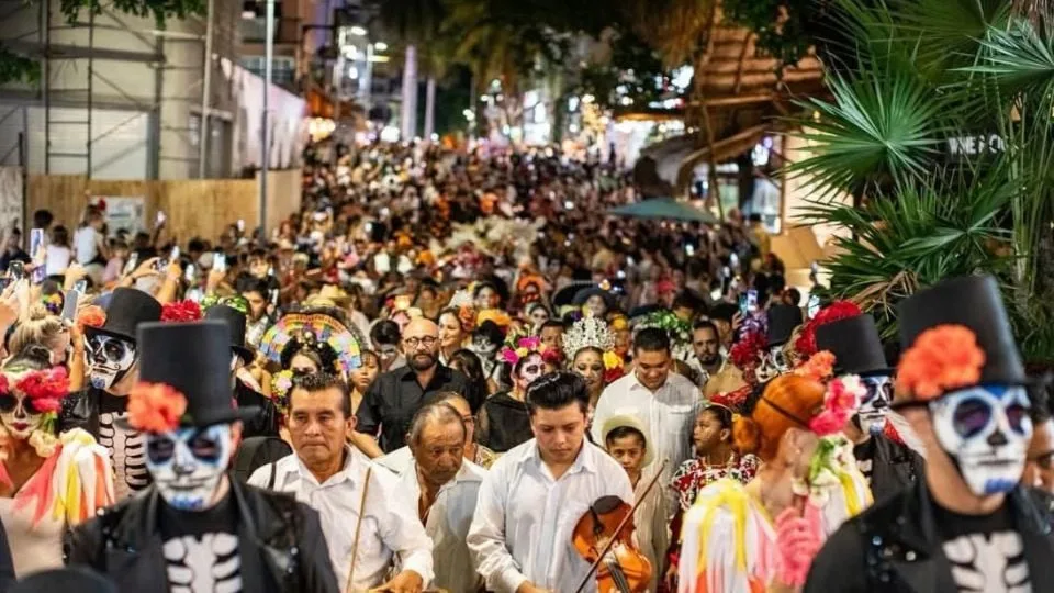 a large crowd dressed in festive attire celebrating Day of the Dead with colorful decorations and face paint in a bustling urban setting