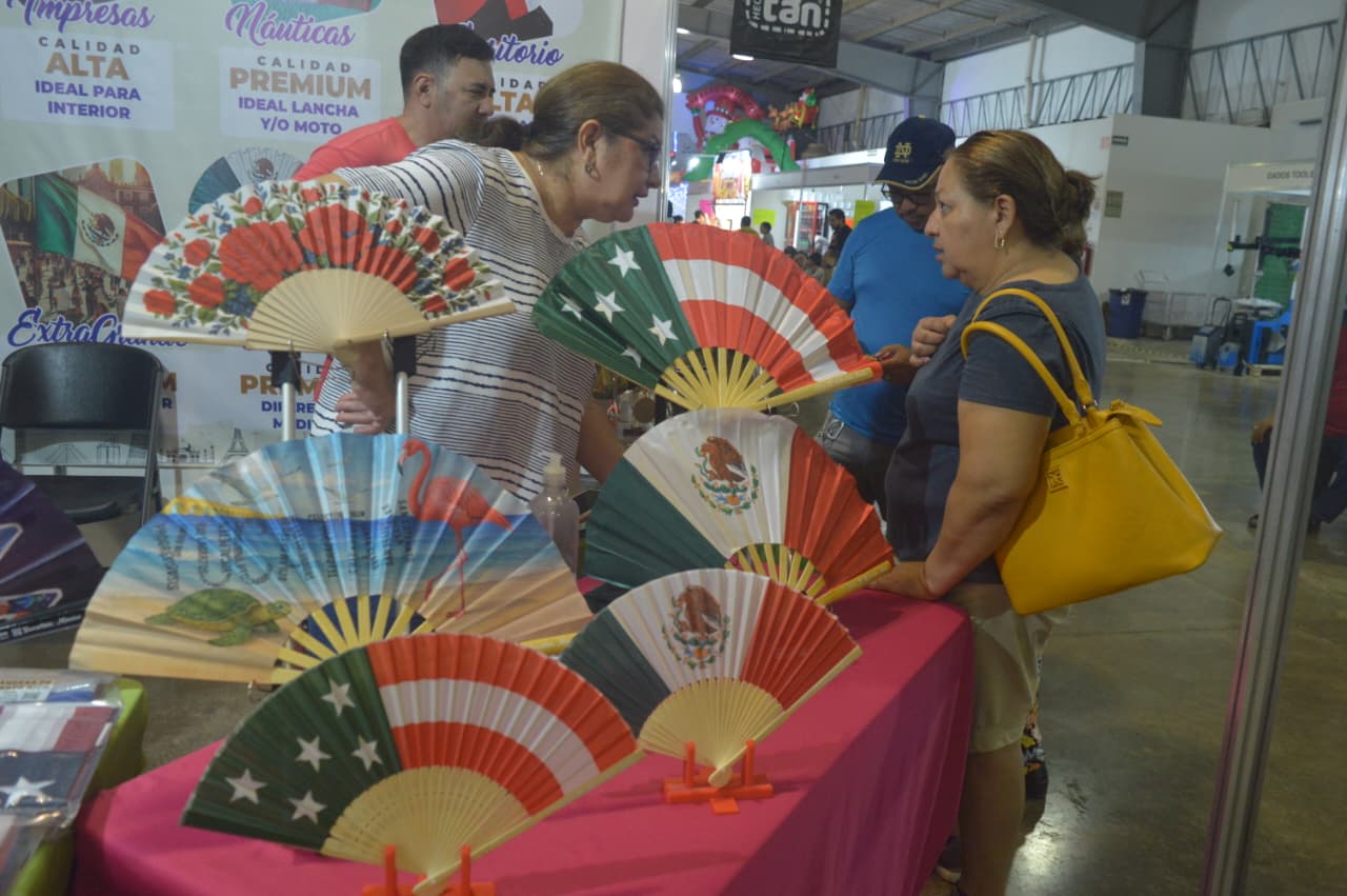 Two women examining colorful decorative fans at a market stall, with various fan designs displayed prominently in front of them.
