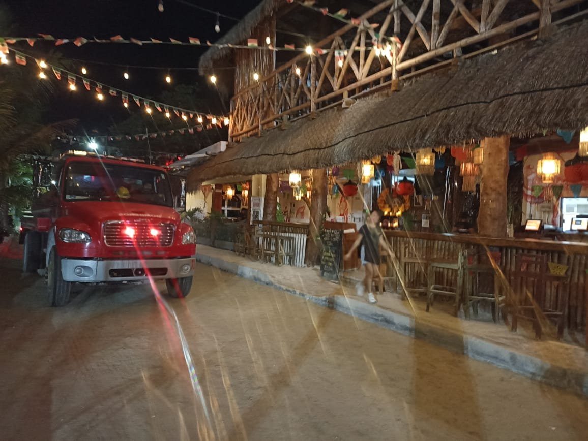 A red truck parked near a lively outdoor restaurant with festive lighting and decorations at night
