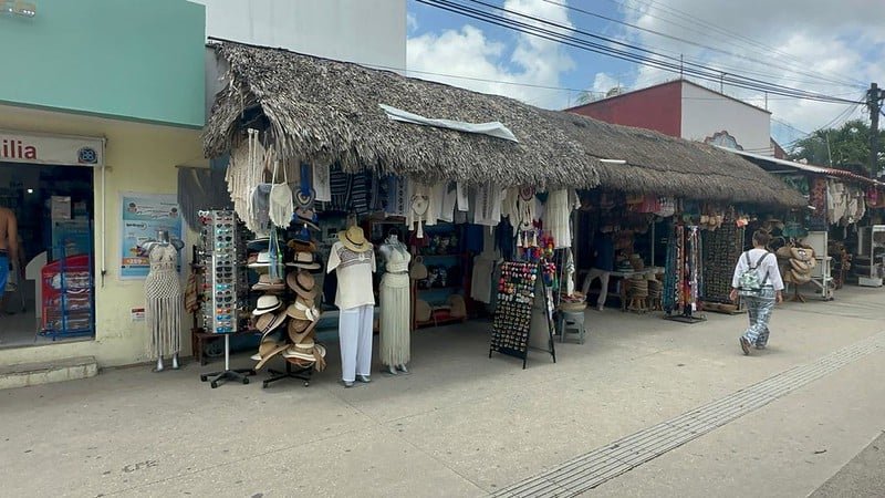 a bustling street market with thatched roof shops displaying clothing accessories and souvenirs in Mexico