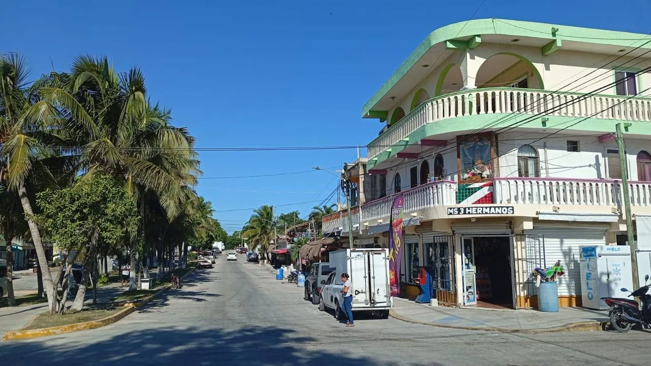 A busy street in a coastal town with palm trees, shops, and clear blue skies