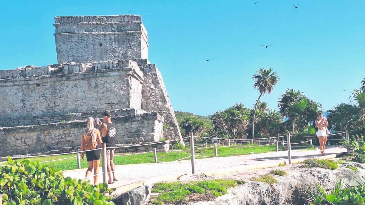 Tourists exploring the ancient Tulum ruins against a clear blue sky.