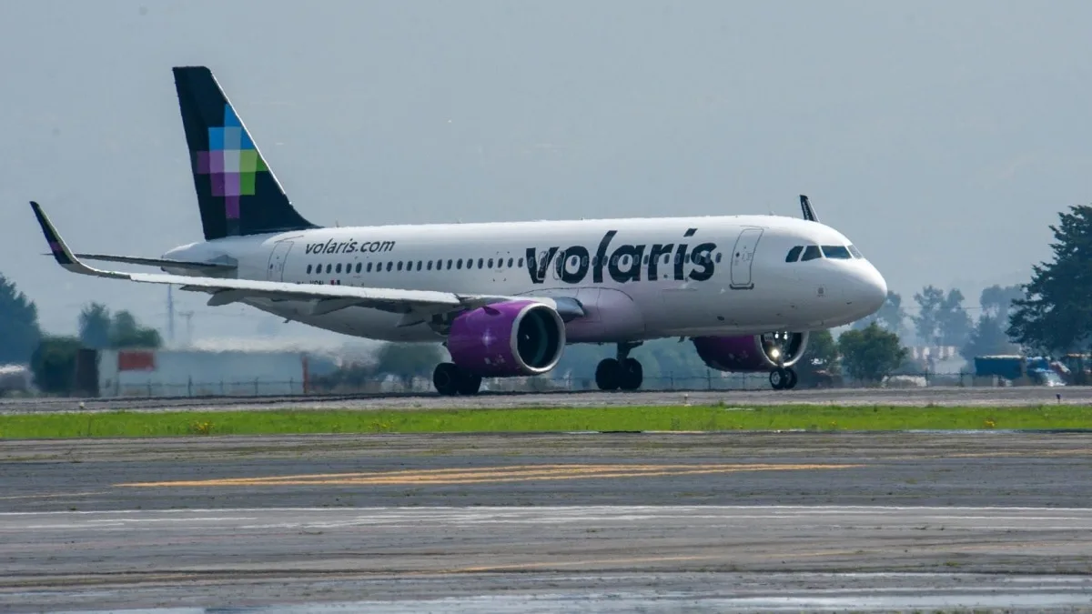 a volaris airplane taxiing on the runway with green grass in the foreground