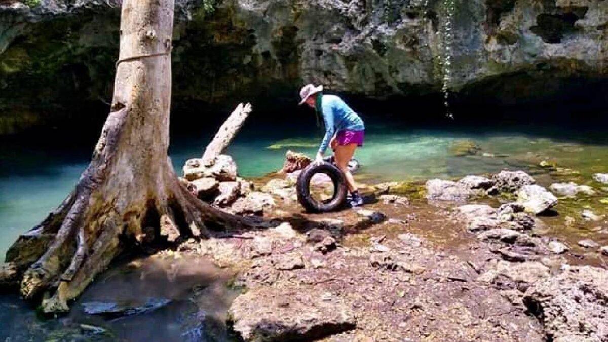 a woman in a blue shirt and pink shorts standing by a river holding a tire-24112025