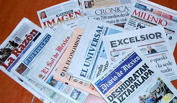 Various Mexican newspapers arranged on a wooden surface, featuring different headlines and logos.$# CAPTION