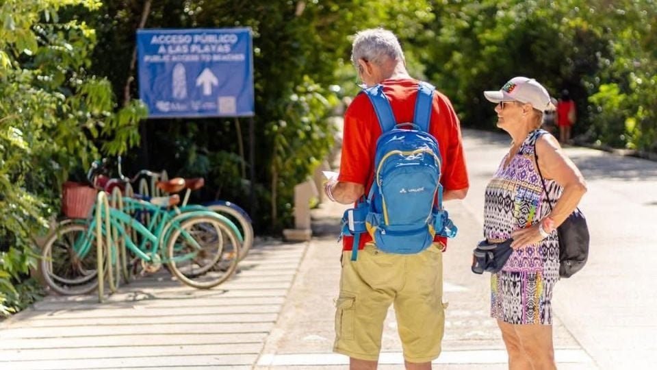 Visitors walking along the beach at Tulum archaeological zone with Mayan ruins in the background
