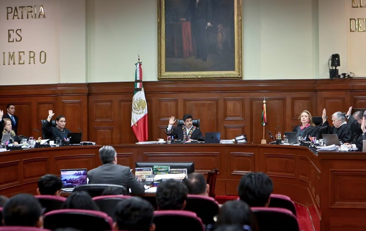 A session in Mexico's Supreme Court with judges raising their hands in a formal setting, a portrait and national flag in the background
