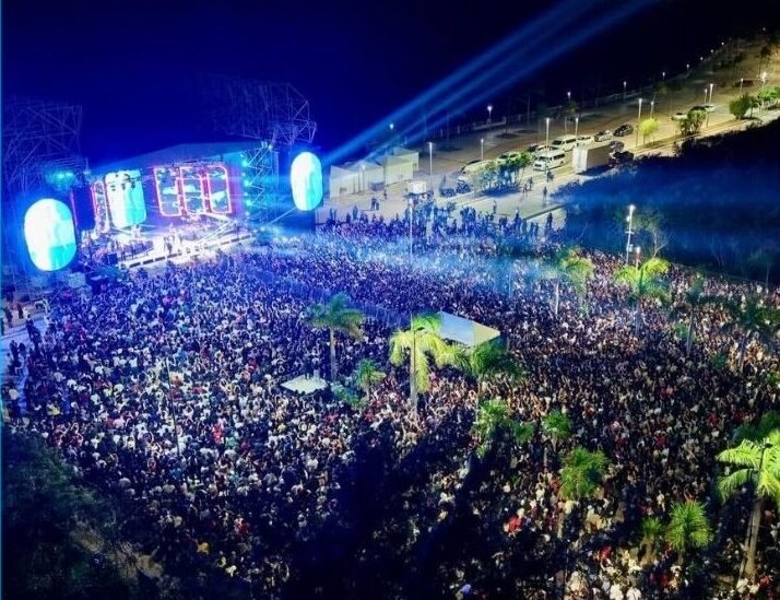 A vibrant scene from Cancún Carnival 2026 showing parade floats and a large crowd at a concert venue